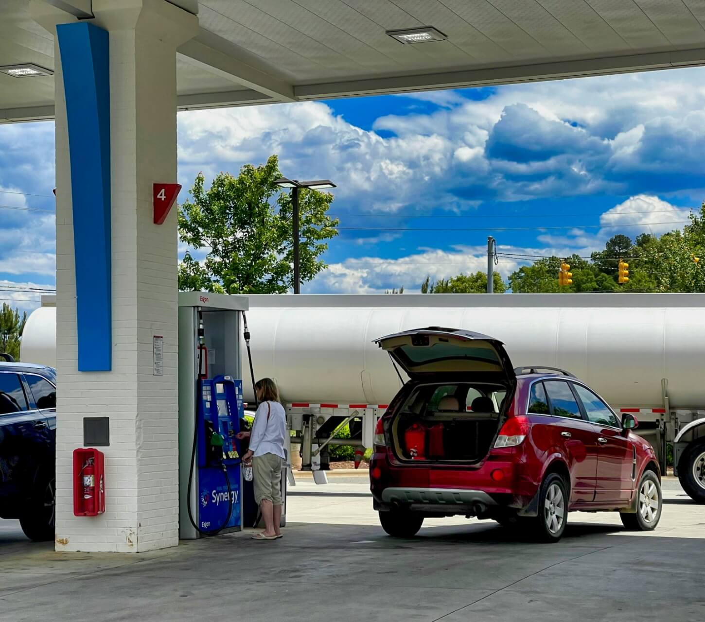 Woman pumping gas at gas station with an oil truck in the background